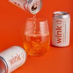 A vibrant image of a canned drink being poured into a glass on an orange studio backdrop.